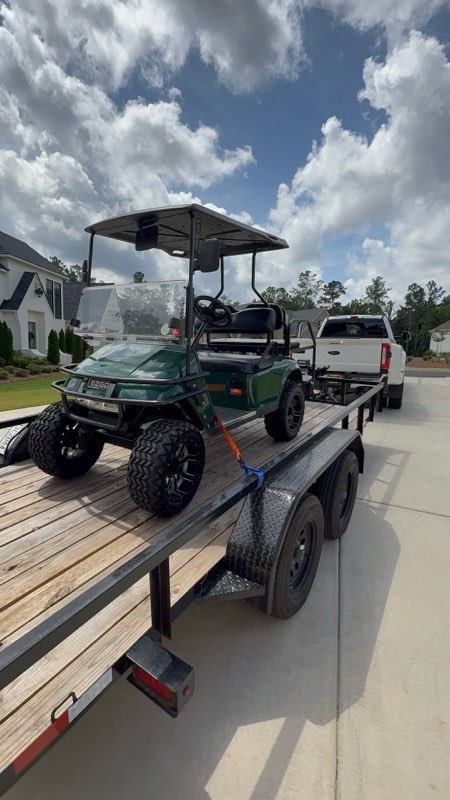 Green E-Z-GO golf cart loaded on a flatbed trailer