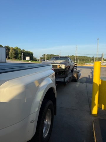 Classic muscle car on a car hauler being towed at dusk